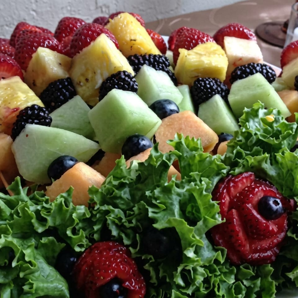 Platter of colorful fruit skewers with strawberries, pineapple, melon, blackberries, blueberries, and lettuce garnish.